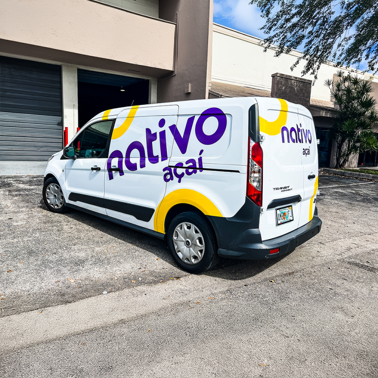 A white commercial van with bold purple and yellow branding for “Nativo Açaí,” parked outside a business complex.